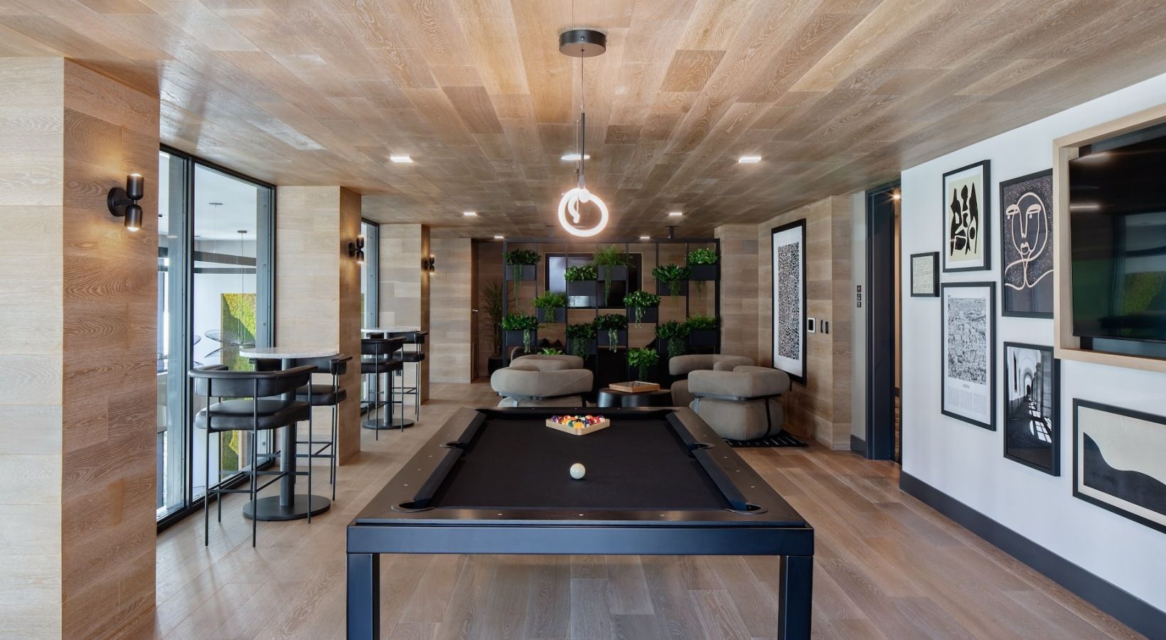 Indoor resident lounge with a pool table, high-top seating by windows, and art on the walls at Sofia, offers apartments for rent in Santa Clara, CA.