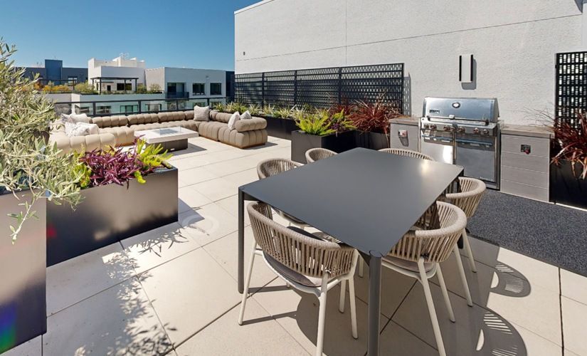 Rooftop outdoor terrace with a dining table, chairs, lounge seating, planters, and a grill at Sofia, offers  pet-friendly apartments in Santa Clara.