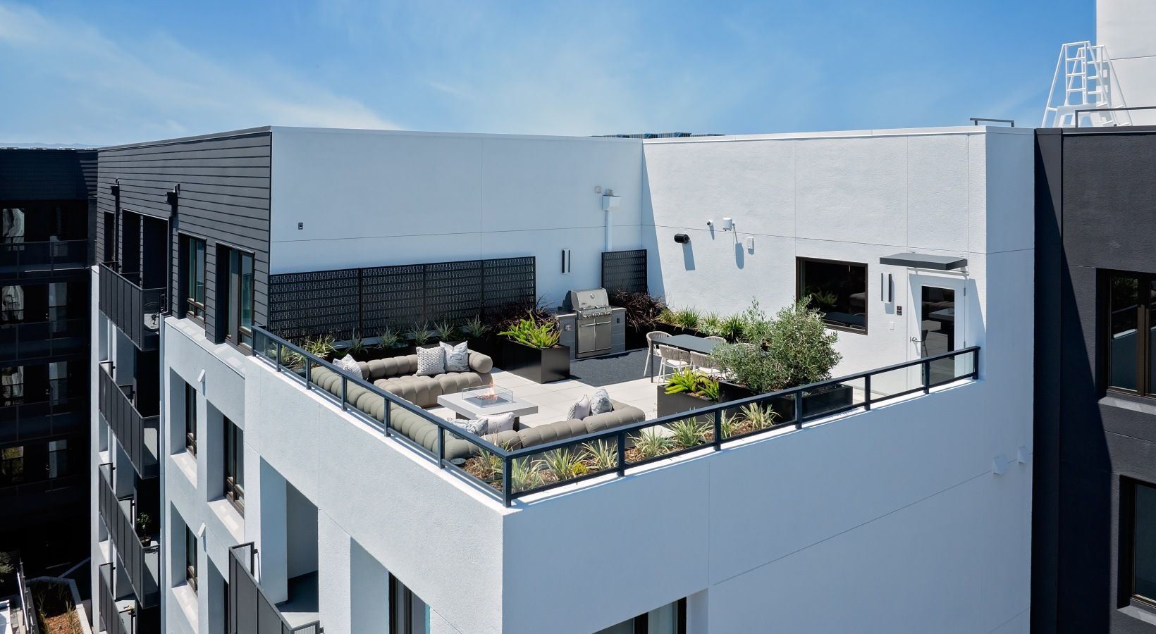 Rooftop terrace with lounge seating, planters, and a grill on a modern apartment building at Sofia in Santa Clara, CA.