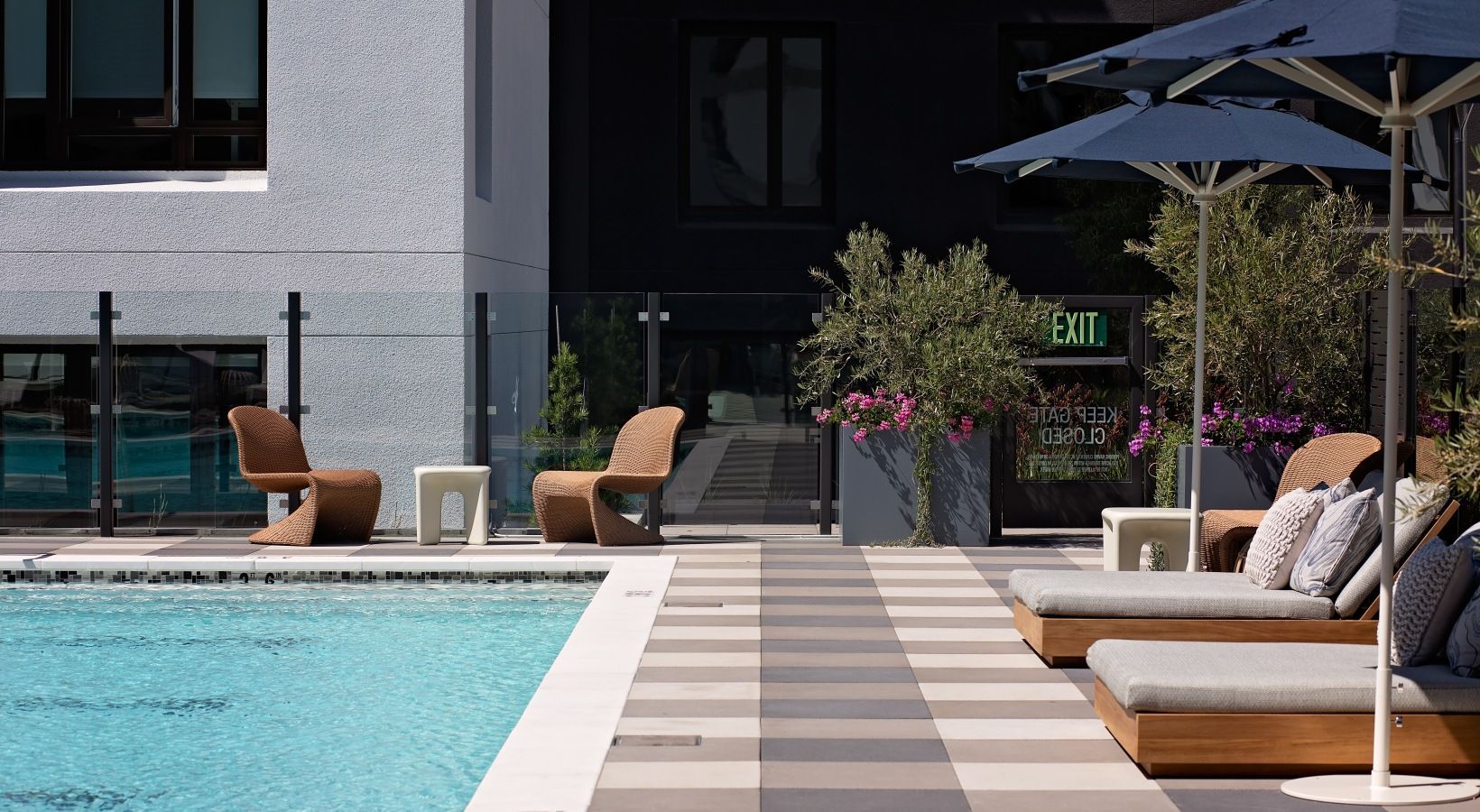 Outdoor pool deck with lounge chairs and umbrellas beside a modern building at Sofia, offers apartments in Santa Clara, CA.