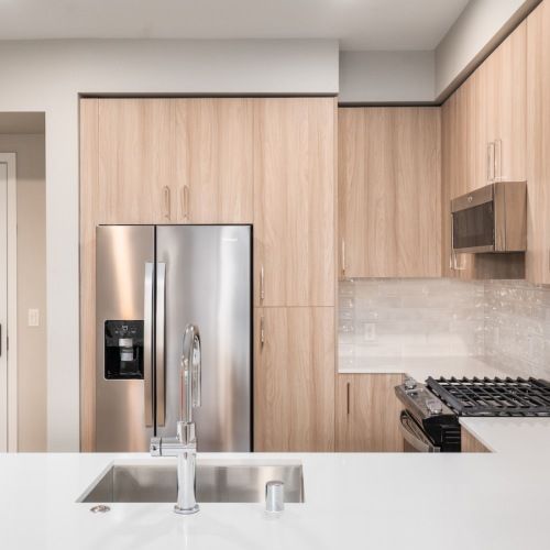 Modern apartment kitchen with stainless steel fridge, light wood cabinets, and a white island at Sofia, offers  pet-friendly apartments in Santa Clara.