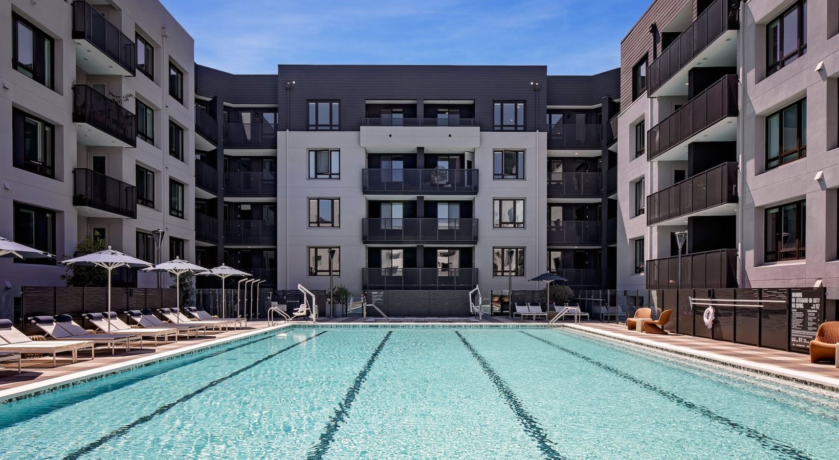 Outdoor apartment community pool with lounge chairs and umbrellas amid modern buildings at Sofia in Santa Clara, CA.