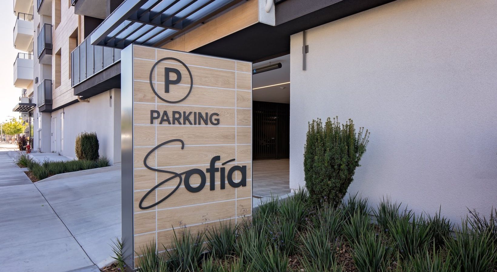 Exterior view of a modern apartment building with a large wooden Parking Sofia sign near the entrance.