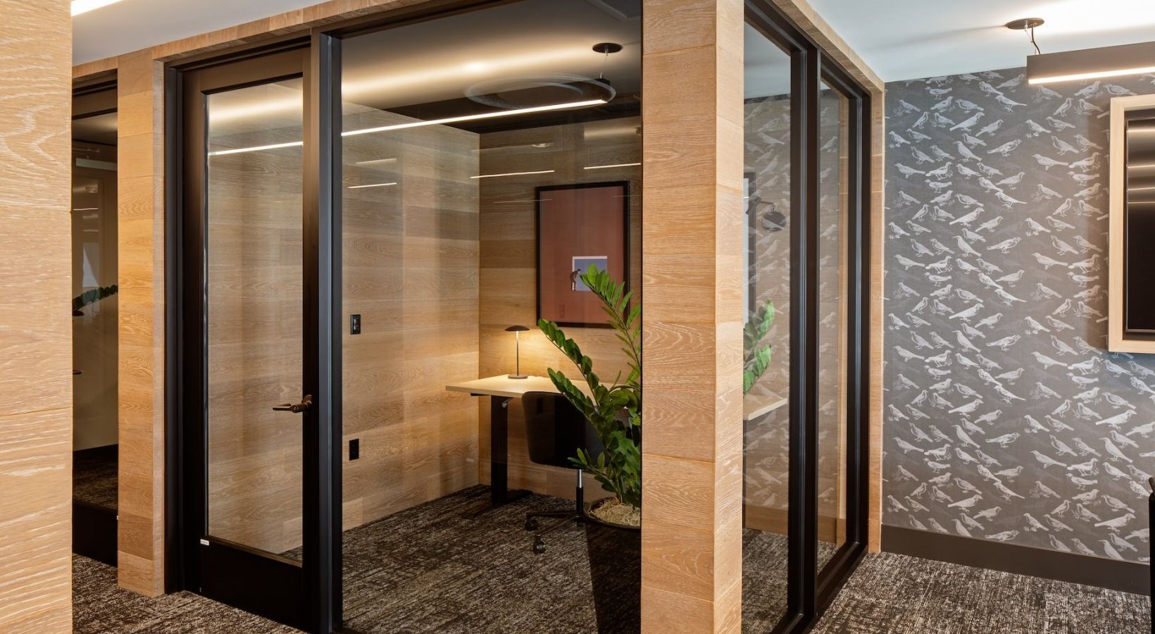 Glass-walled private office in a wood-paneled lobby, with a desk, chair, lamp, and plant at Sofia, offers apartments for rent in Santa Clara, CA.