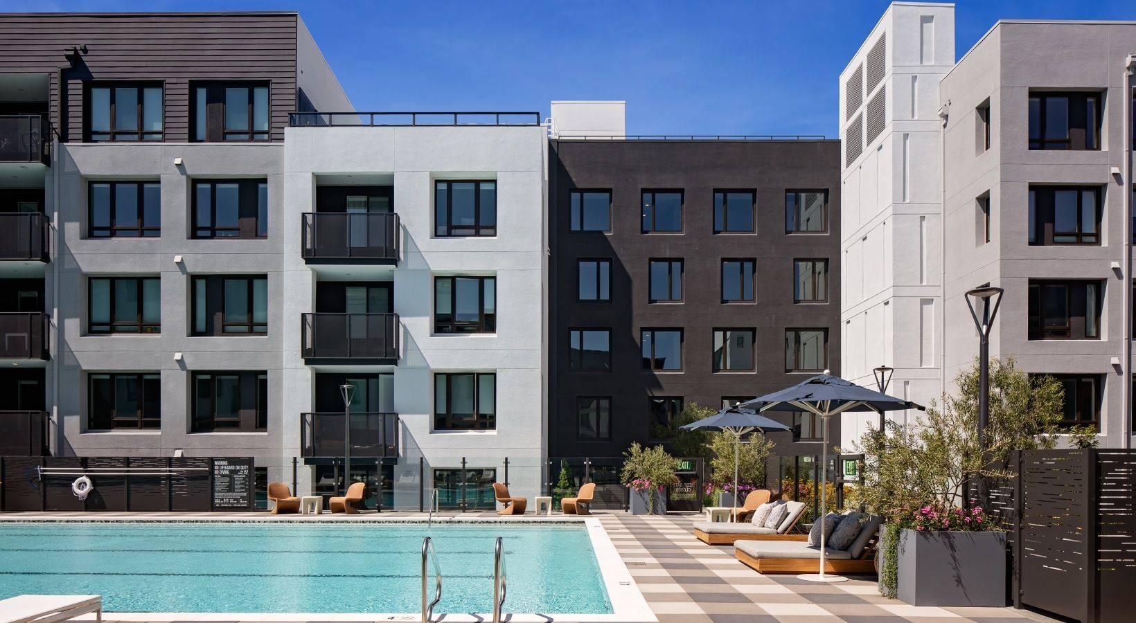 Outdoor pool deck with lounge chairs, umbrellas, and modern apartment buildings at Sofia in the background.
