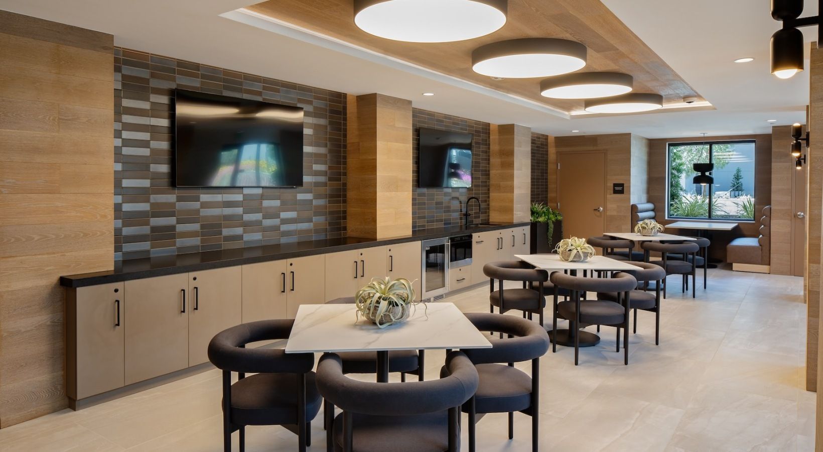 Modern community lounge with kitchenette, tables, and wall-mounted TV at Sofia, offers apartments for rent in Santa Clara, CA.