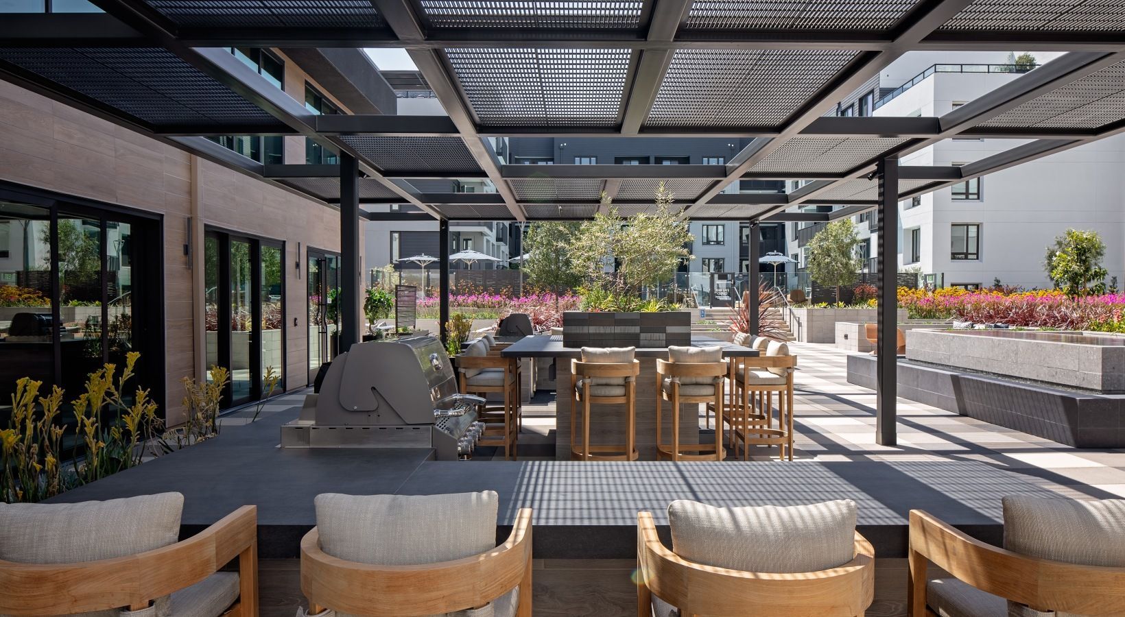 Outdoor community amenity terrace with a grill, high-top tables, and lounge seating under a pergola at Sofia, offer apartment living in Santa Clara, CA.