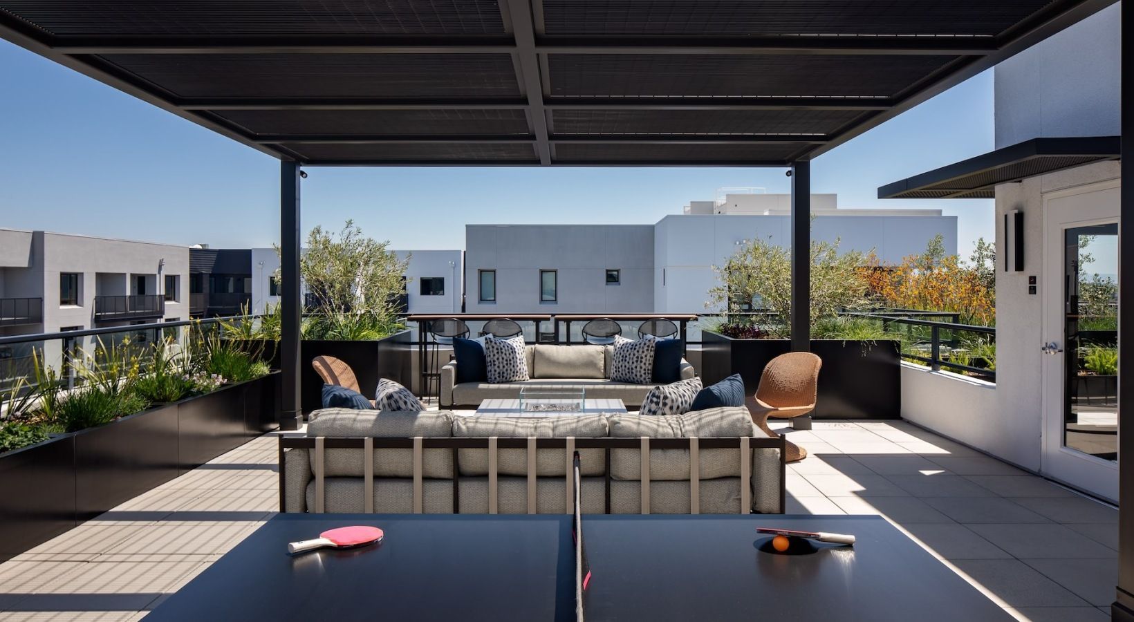 Rooftop outdoor lounge with beige sectional sofas, throw pillows, and chairs under a dark pergola at Sofia, offers Santa Clara apartments for rent in CA.