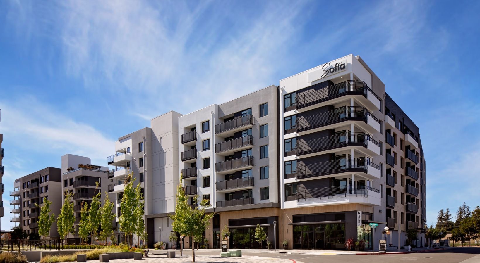 Exterior view of a modern multi-story apartment building with balconies and storefronts at Sofia in Santa Clara, CA.