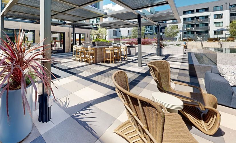 Outdoor communal patio with wicker lounge chairs, high-top tables under a pergola, near a pool at Sofia, offers  pet-friendly apartments in Santa Clara.