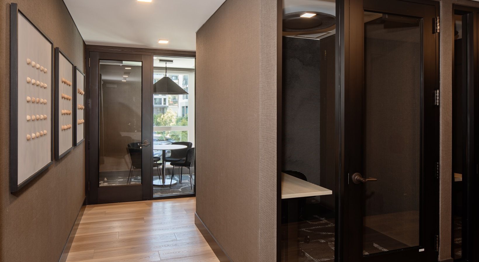 Interior hallway with glass-door meeting room and private phone booths at Sofia, offers apartments in Santa Clara, CA.