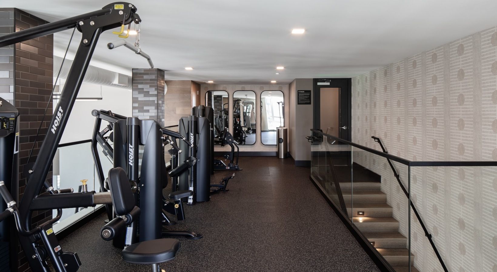 Gym with weight machines and stairs leading up. Dark color scheme, interior setting.