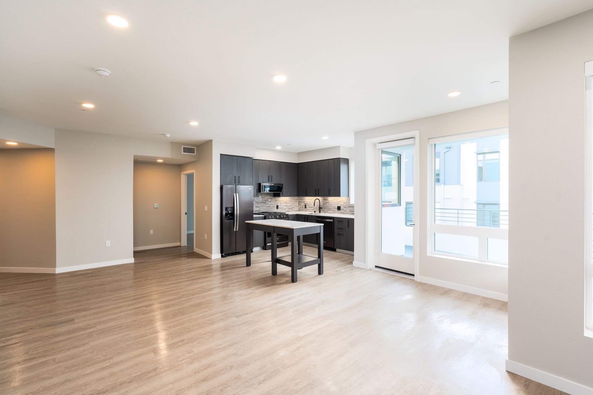 Open-concept modern living space with kitchen and large windows, wood floors, and neutral walls at Sofia, offers apartments in Santa Clara.