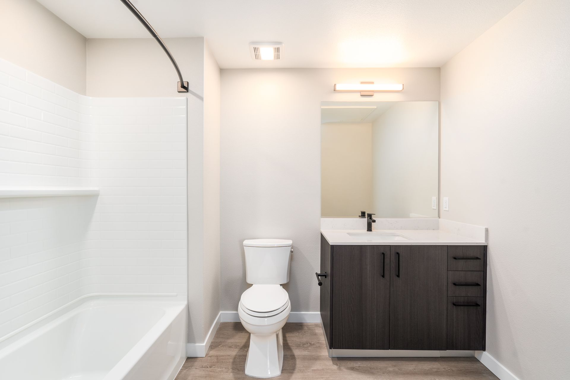 Bathroom with white tub, toilet, dark cabinet, mirror, and light fixture at Sofia, offers studio, 1, and 2 bedroom apartments in Santa Clara, CA.