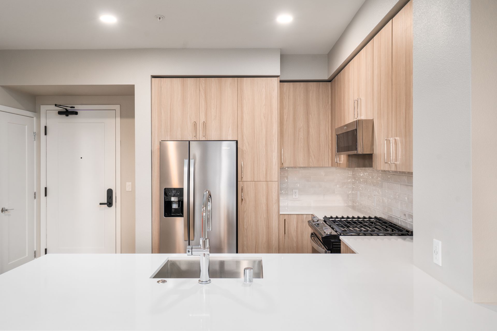 Modern kitchen with white countertops, stainless steel appliances, and light wood cabinets at Sofia, offers apartments in Santa Clara.