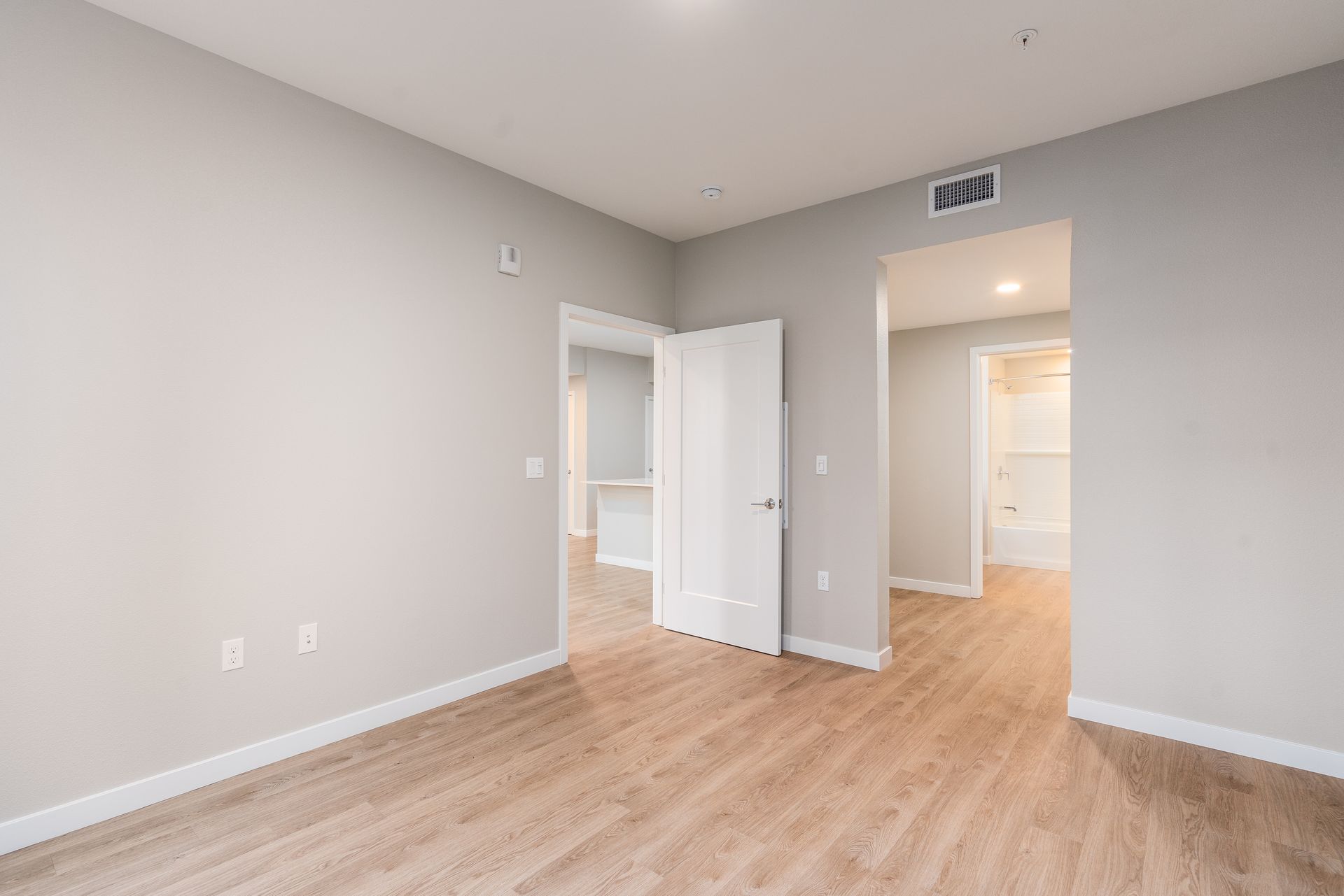 Empty bedroom with neutral walls, wood-look flooring, and three doorways at Sofia, offers studio, 1, and 2 bedroom apartments in Santa Clara, CA.