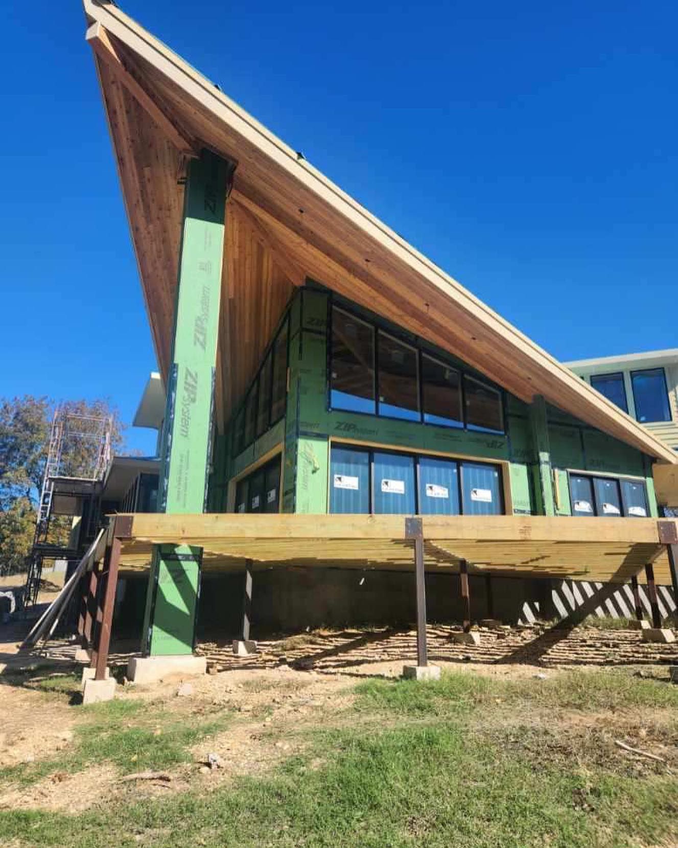 A large house is being built on a hill with a wooden deck.