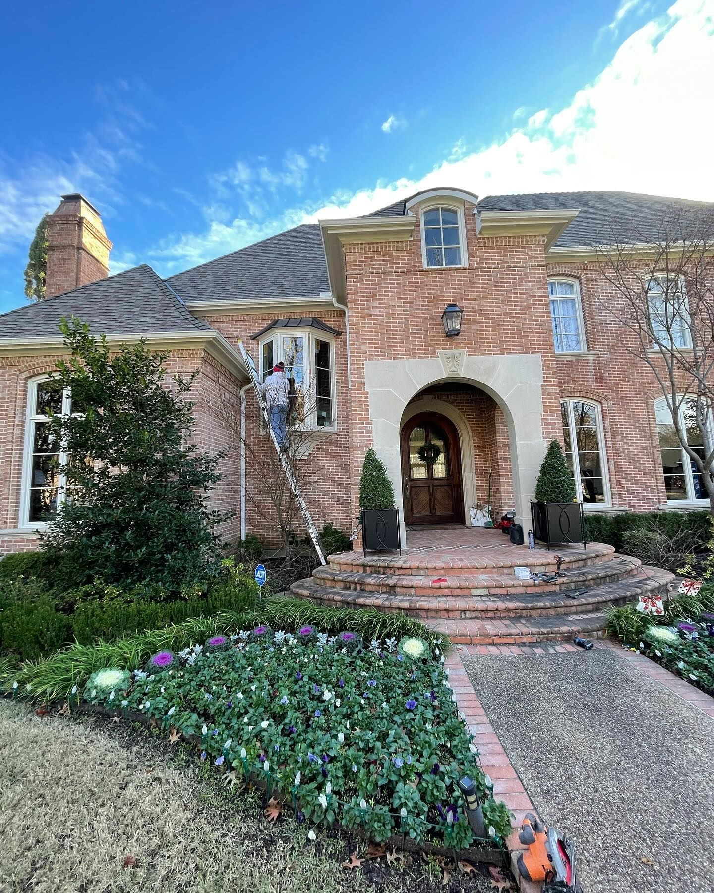 A man is standing on a ladder in front of a large brick house.
