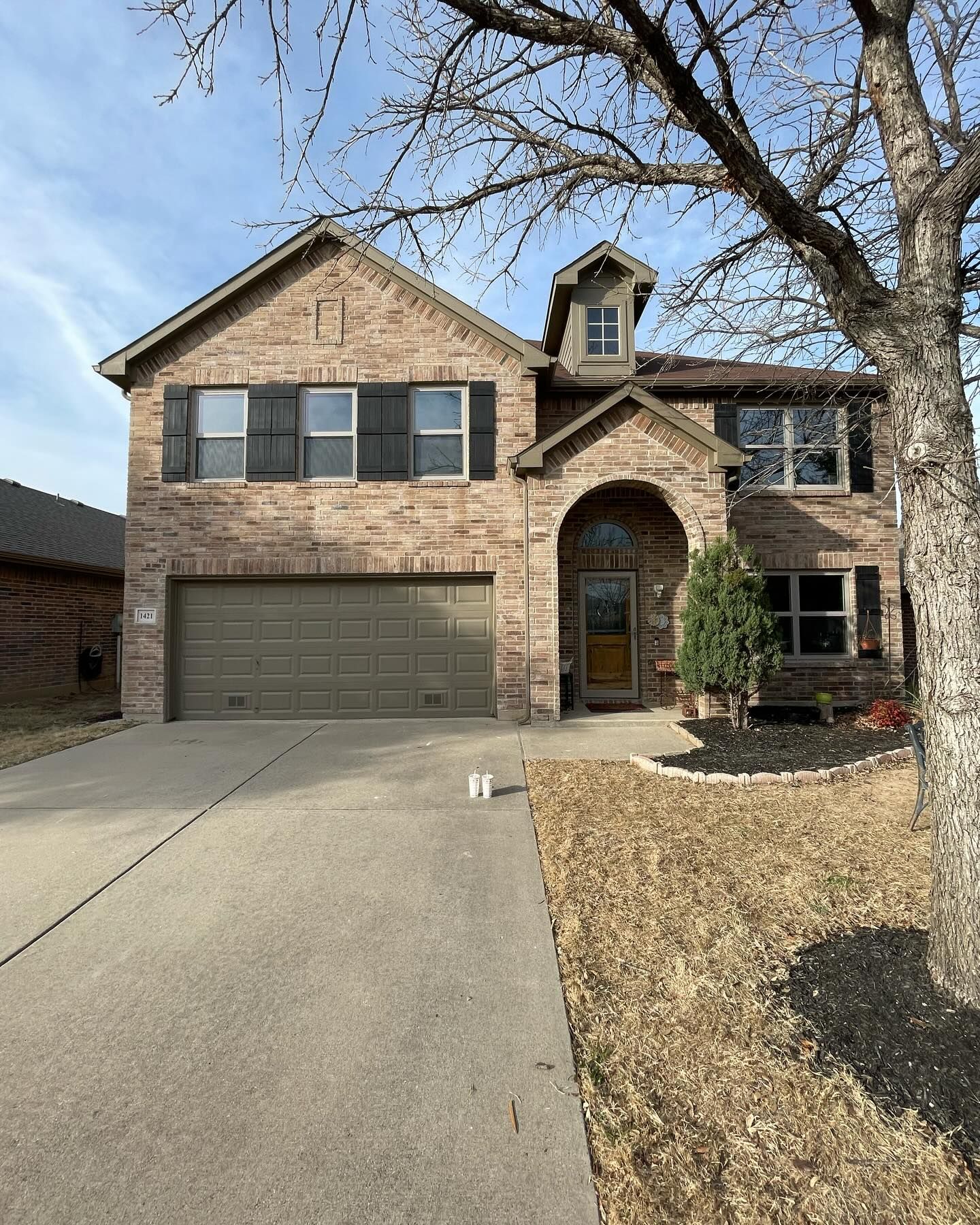 A large brick house with a garage and a tree in front of it.