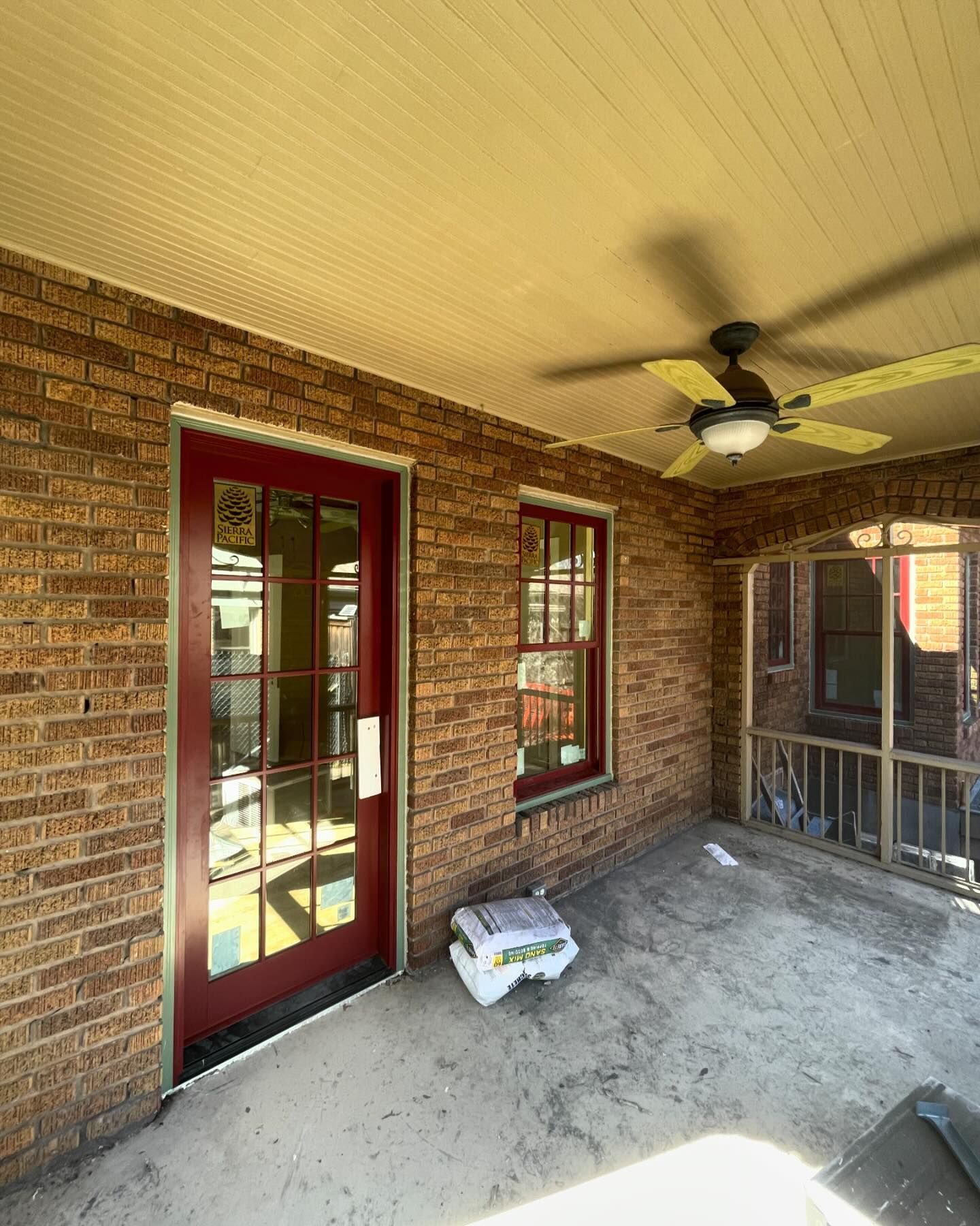 A brick porch with a red door and a ceiling fan