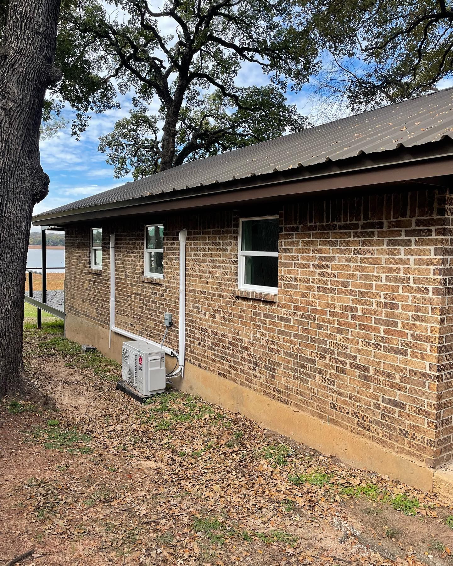 A brick house with a metal roof and a tree in front of it.