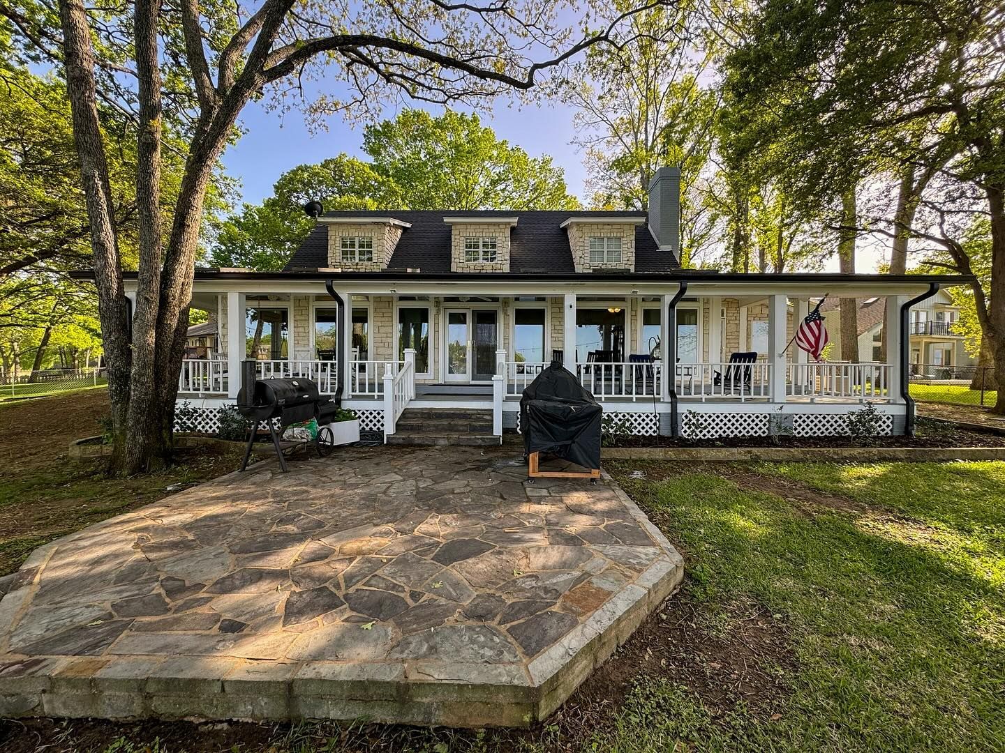 A large white house with a large porch and patio surrounded by trees.