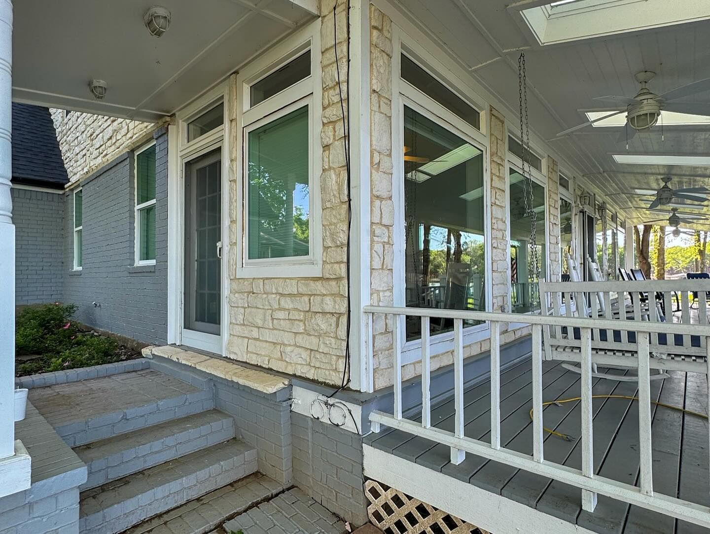 The porch of a house with a lot of windows and a ceiling fan.
