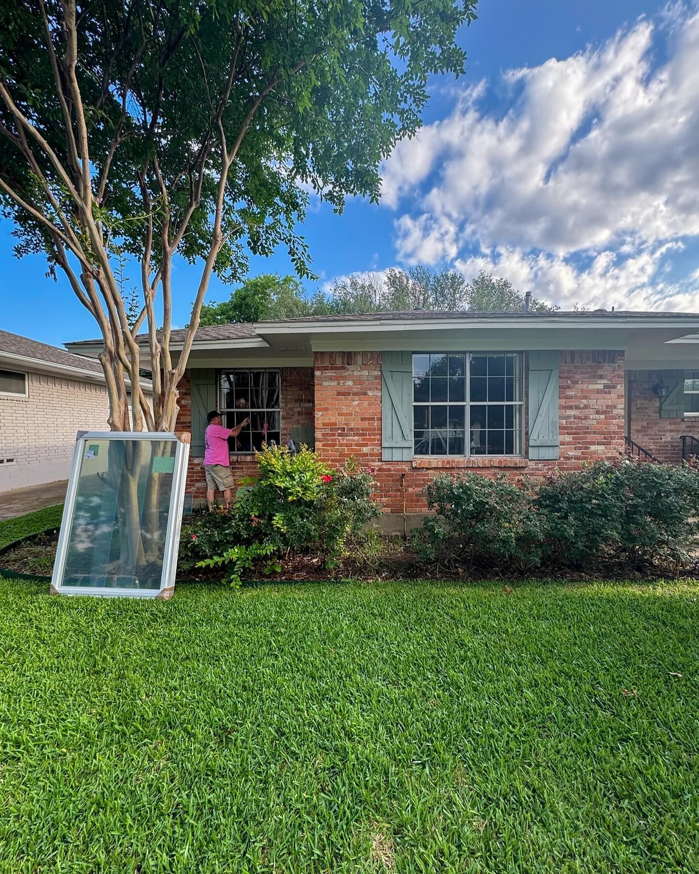 A woman is standing in front of a brick house with a window.