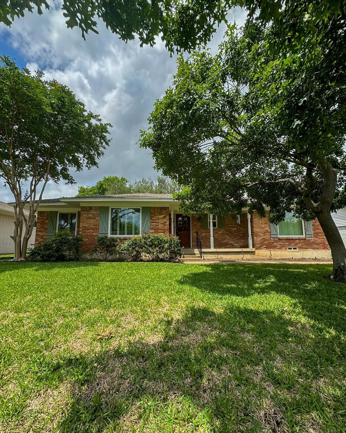 A brick house with a large lawn and trees in front of it.