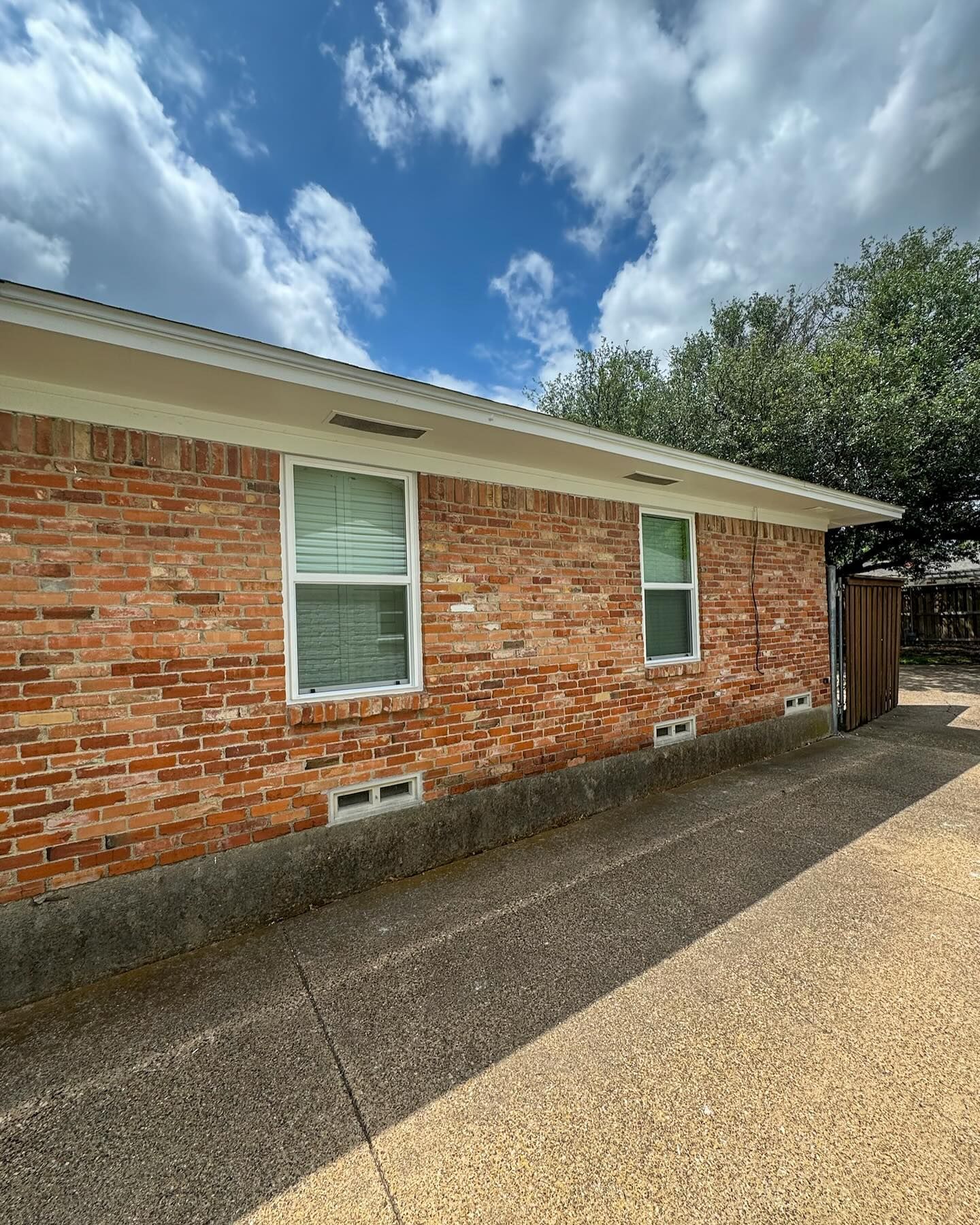 A brick house with two windows and a driveway in front of it.