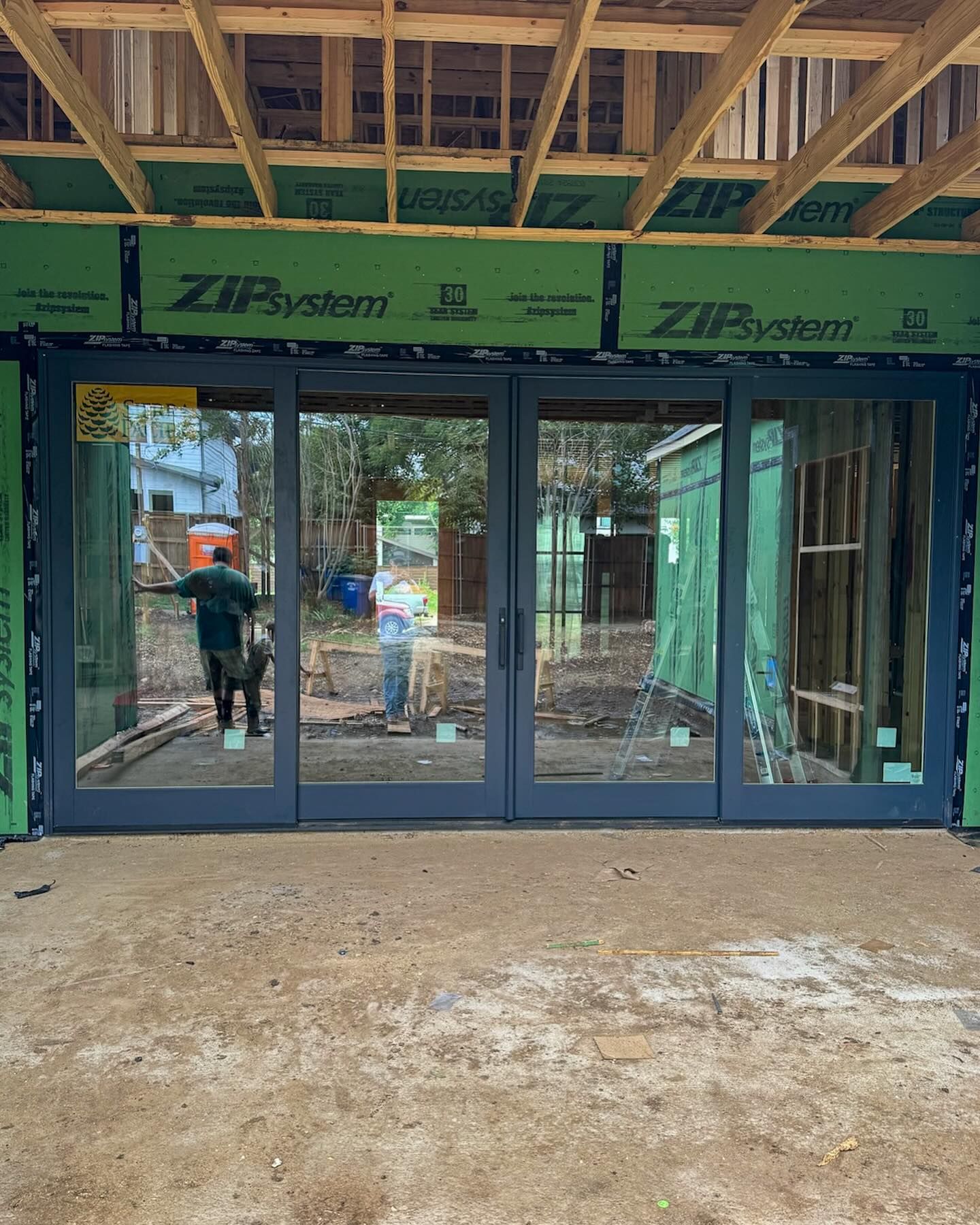 A man is standing in front of a large glass door in a building under construction.