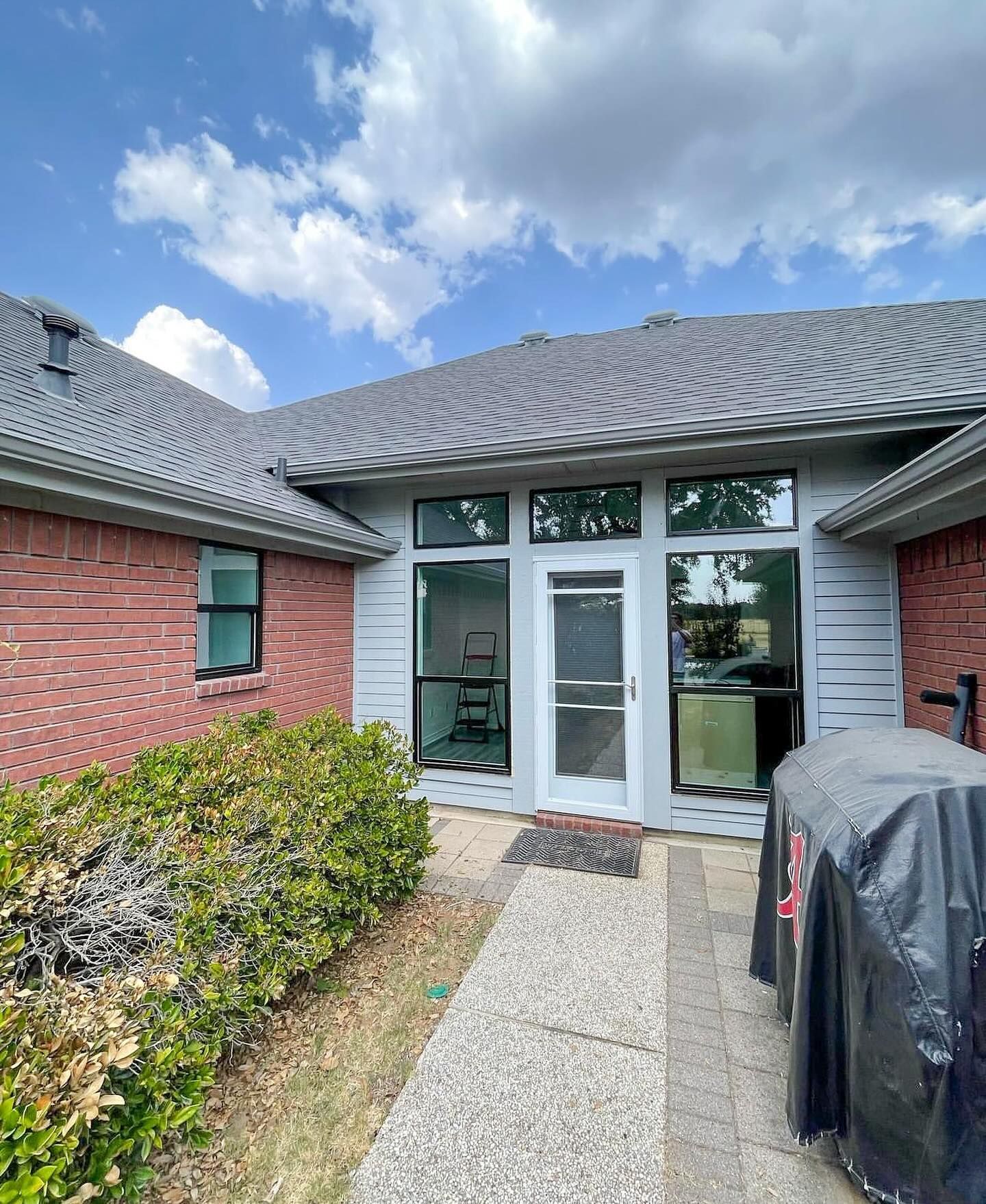 A brick house with a white door and a grill in front of it.