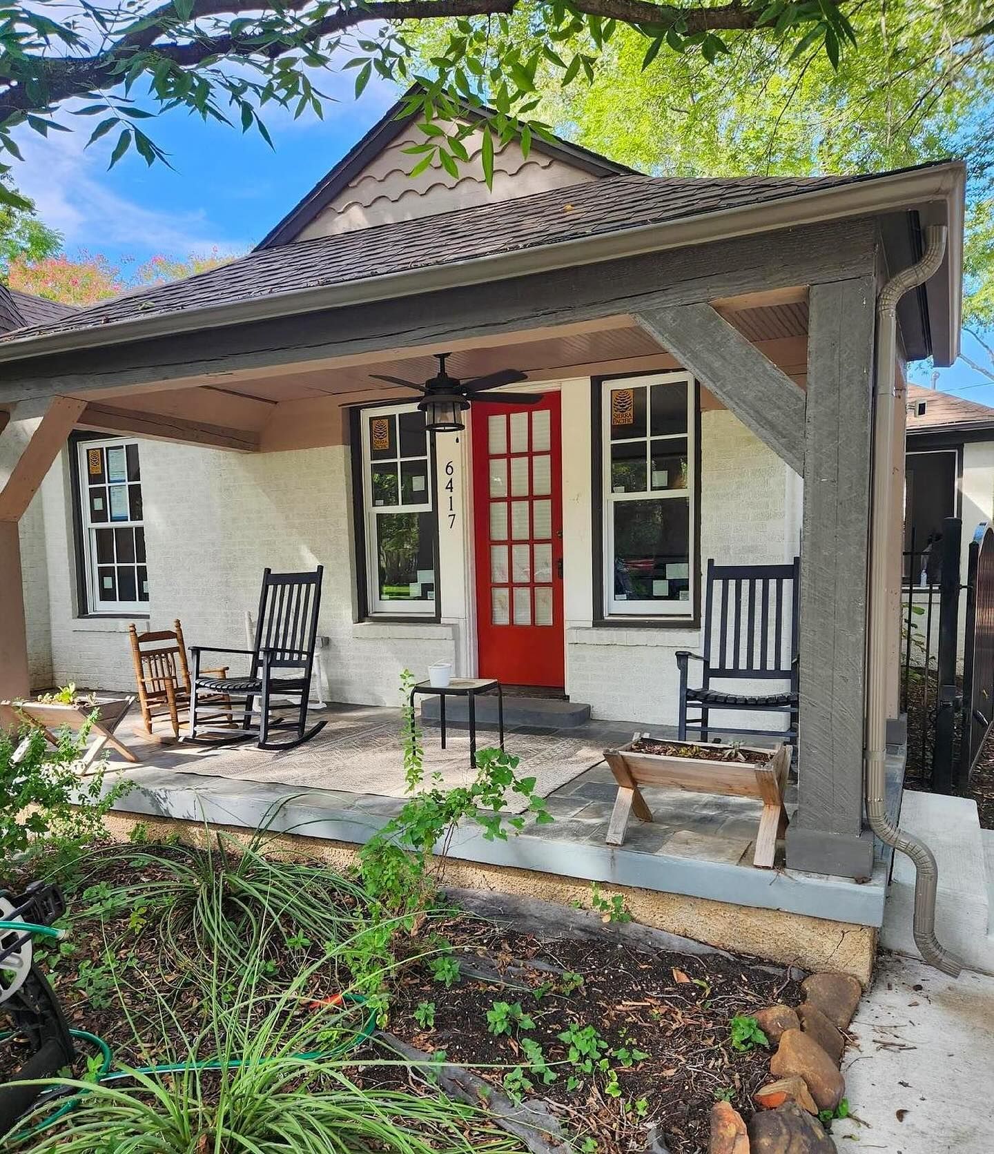 A white house with a red door and rocking chairs on the porch.