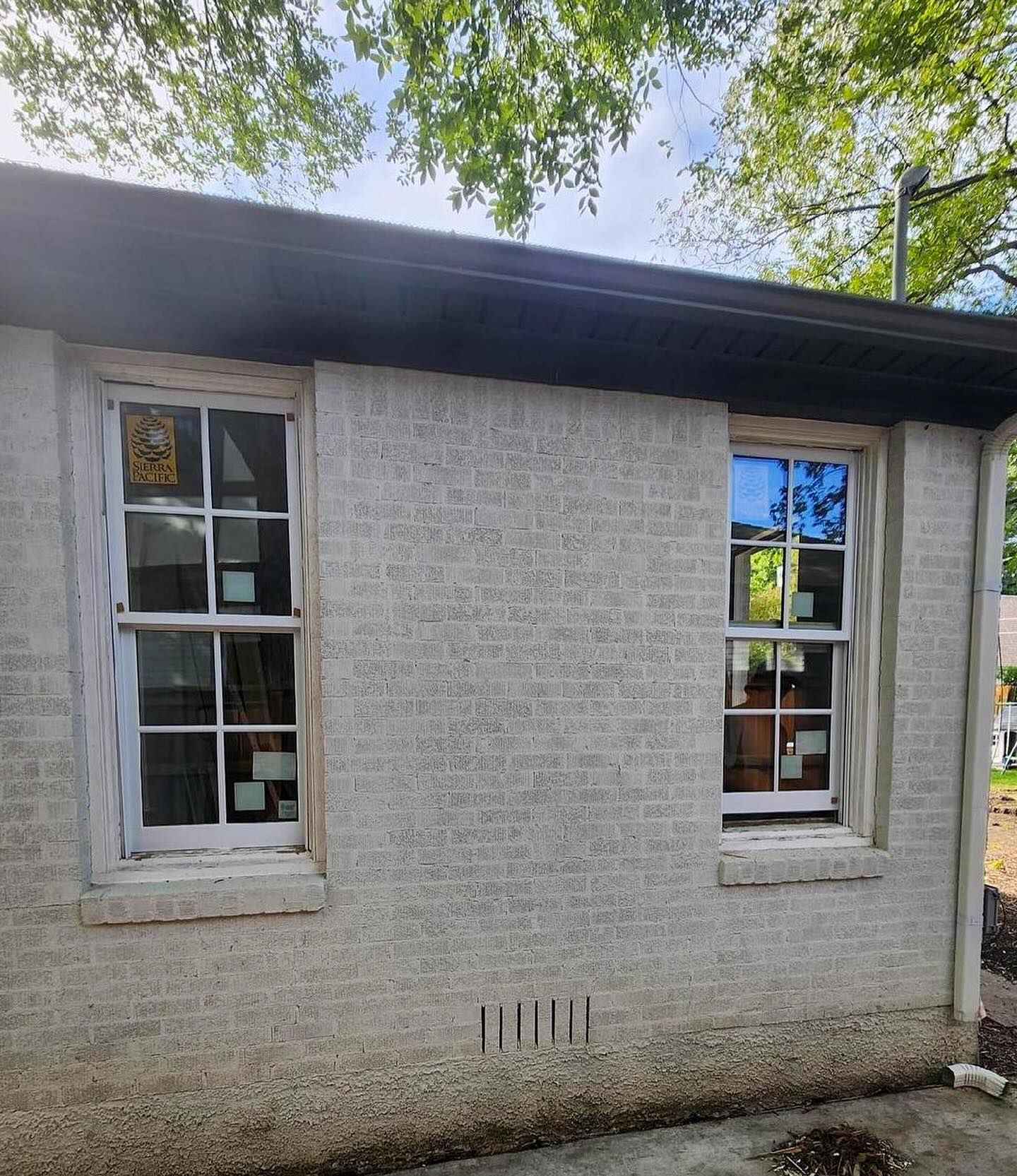 A white brick building with two windows and a black roof.