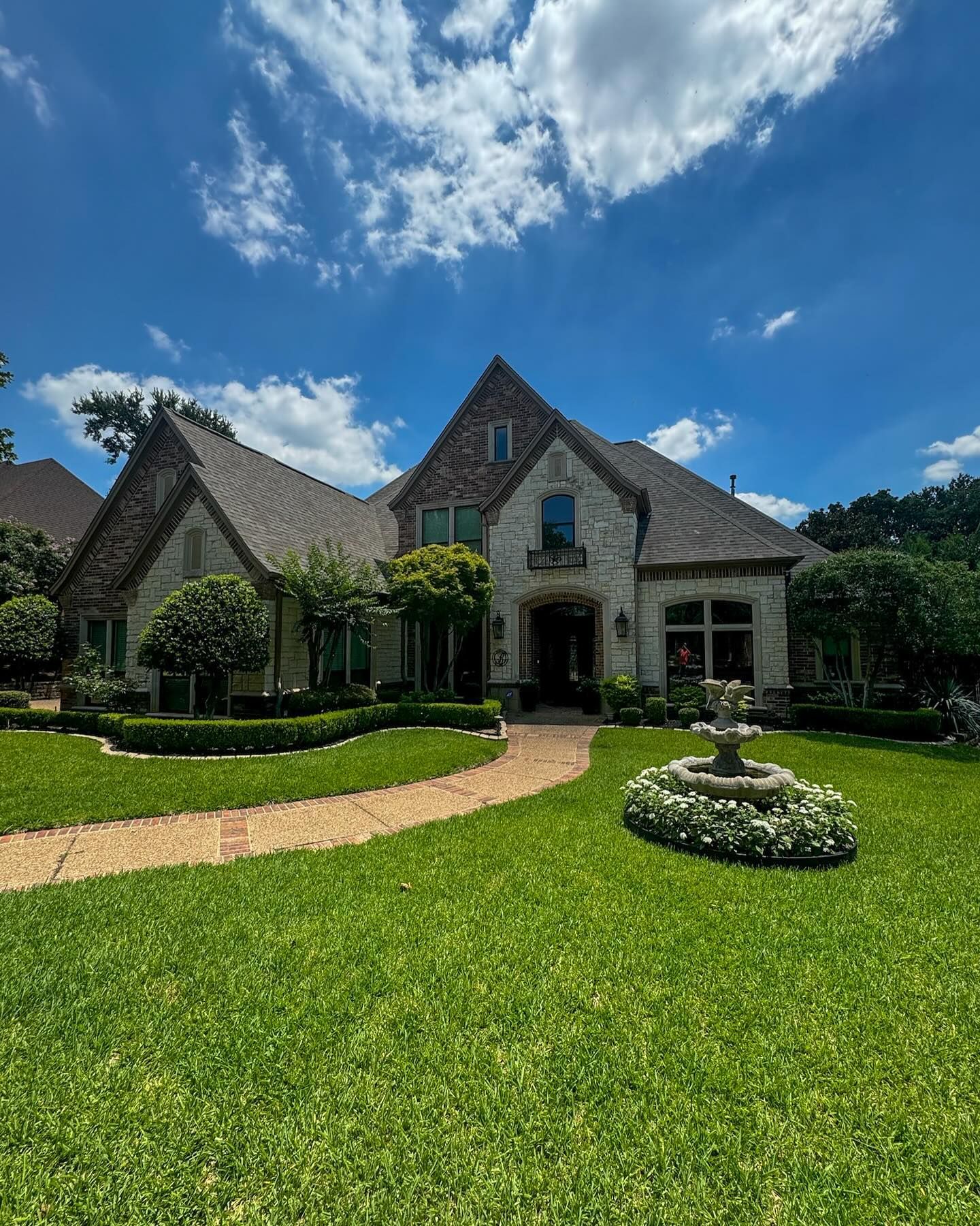 A large house with a lush green lawn and a fountain in front of it.