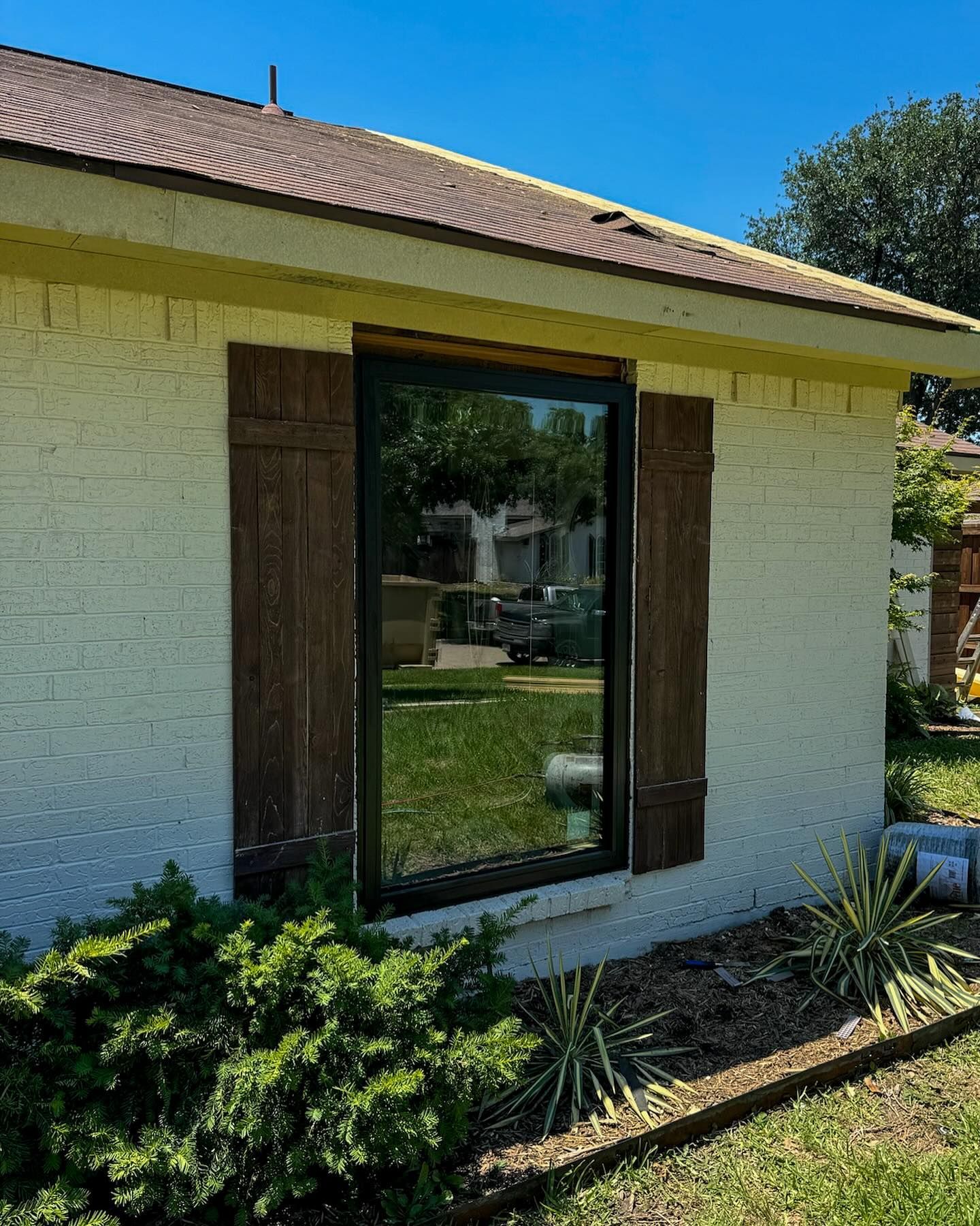 A white brick house with a large window and brown shutters.
