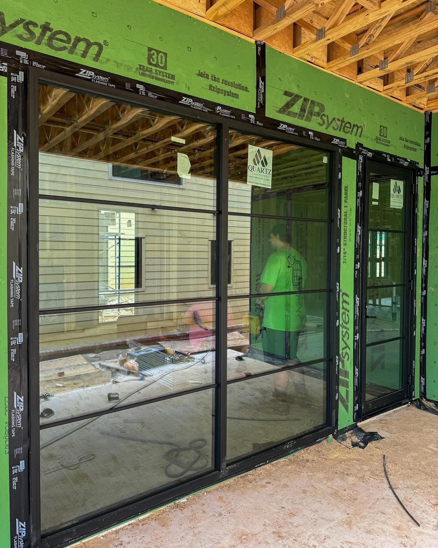 A man in a green shirt is standing in a room with a lot of windows.