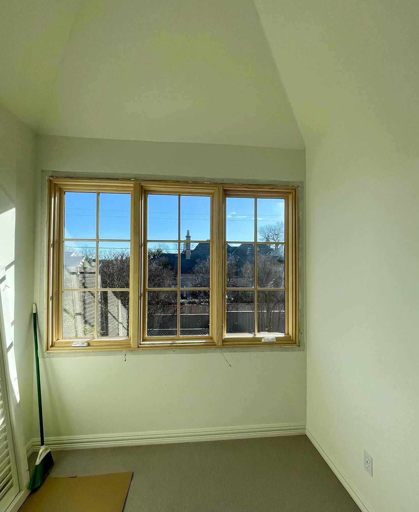 A room with three windows and a broom on the floor