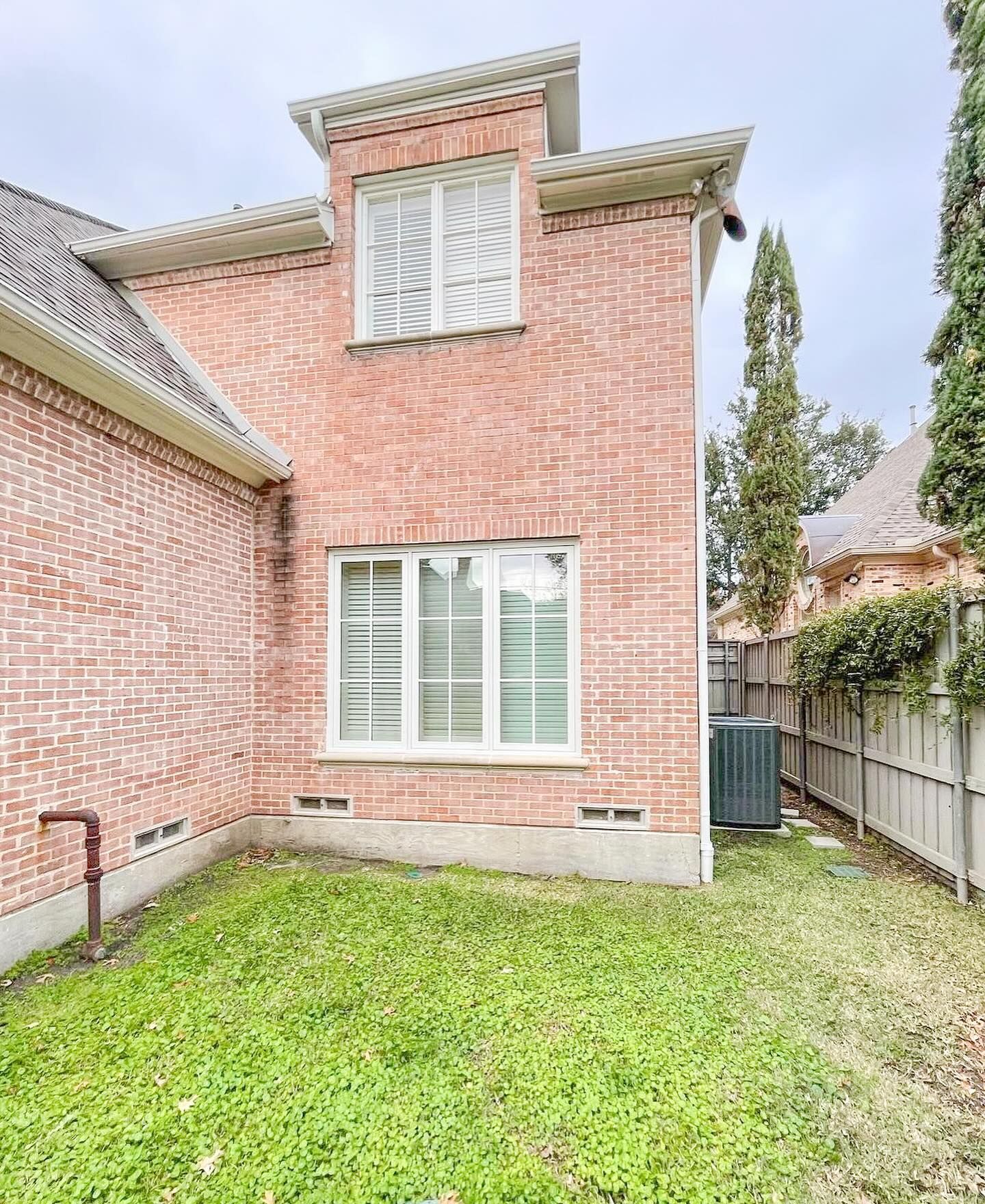 The backyard of a brick house with a large lawn and a fence.
