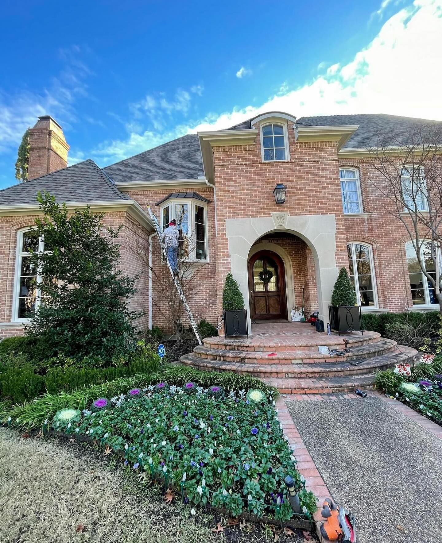 A man is standing on a ladder in front of a large brick house.