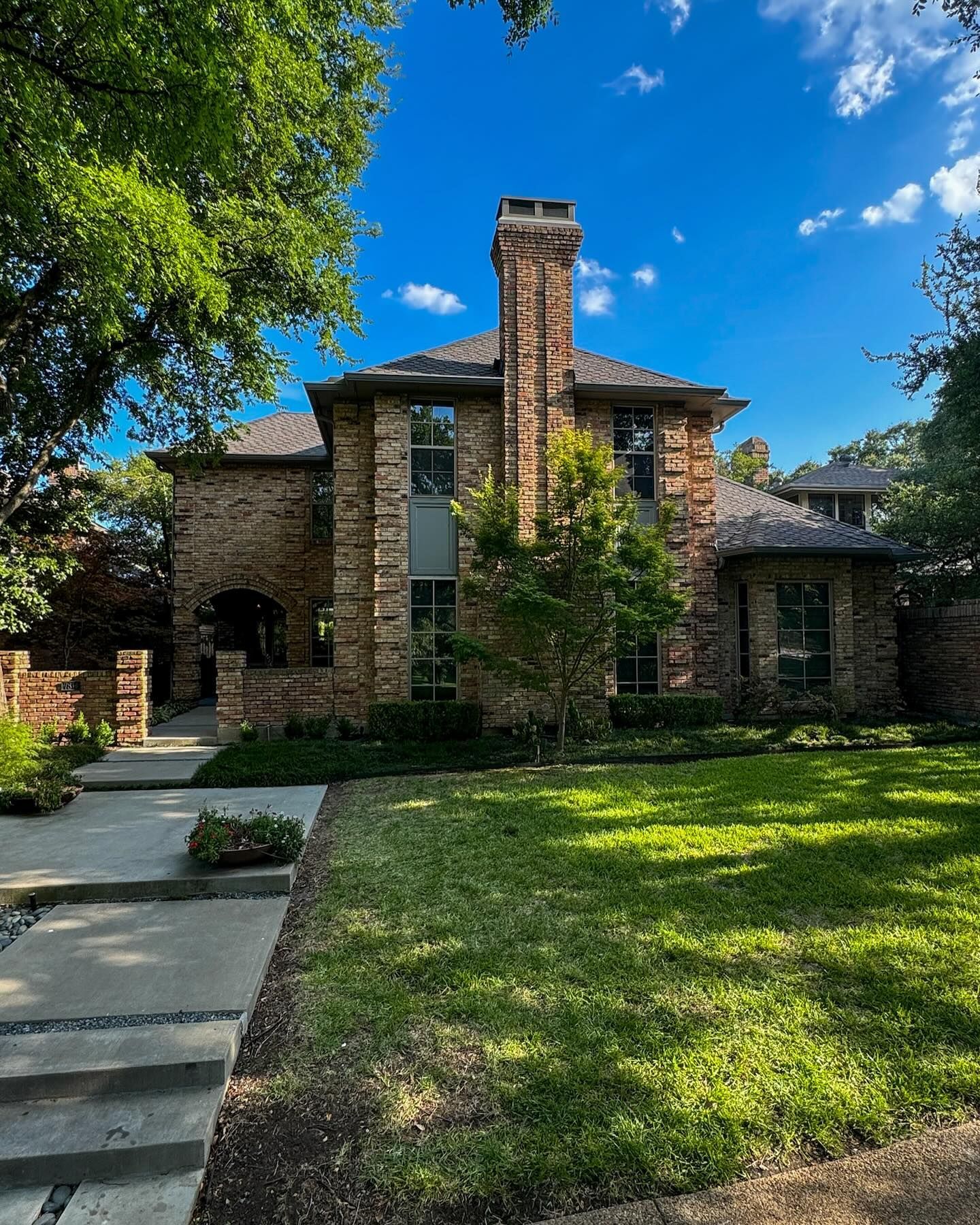 A large brick house with a chimney and a lush green lawn.