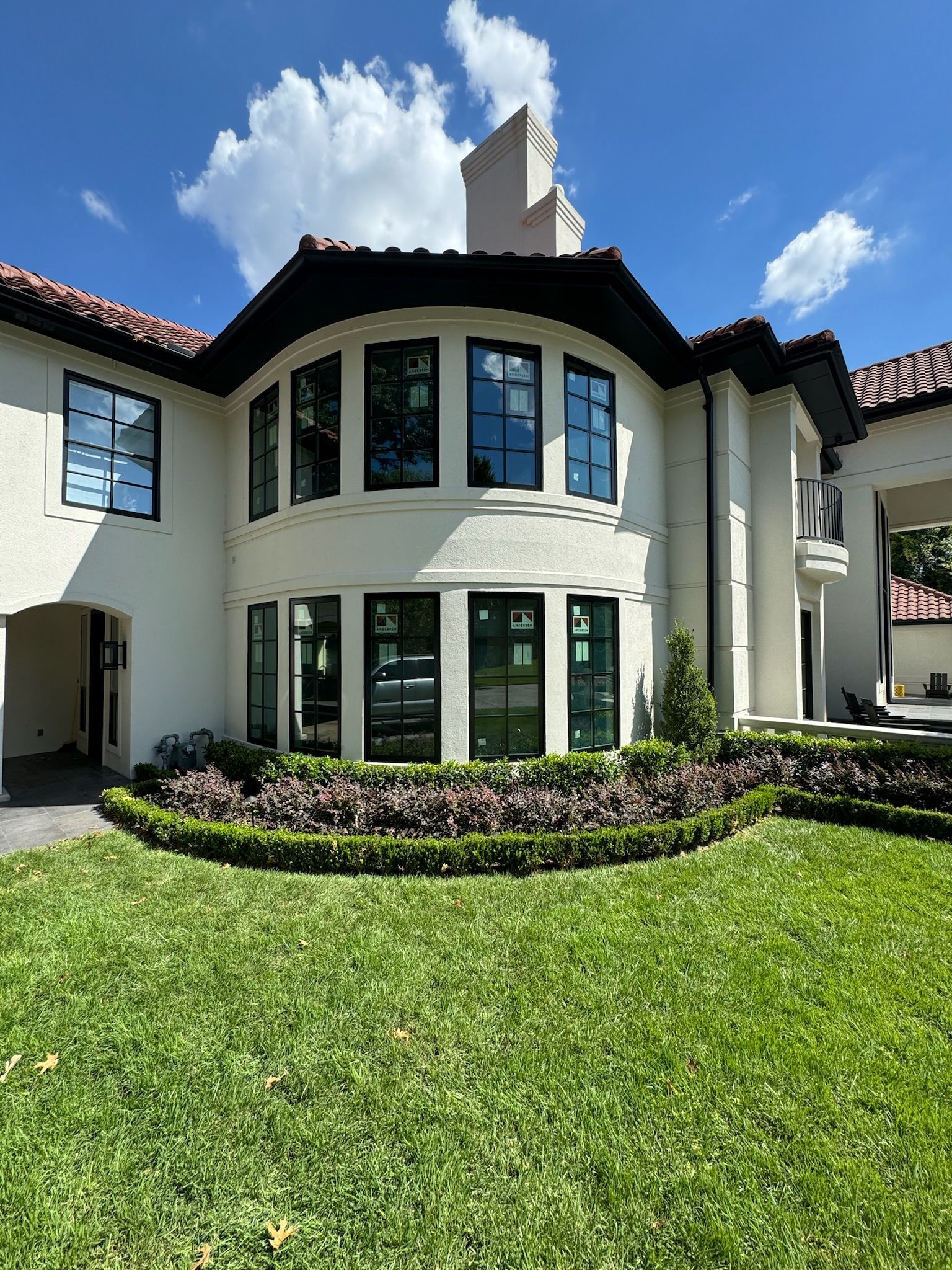 Front view of a white two-story house with curved windows, red roof, and green lawn under a blue sky.