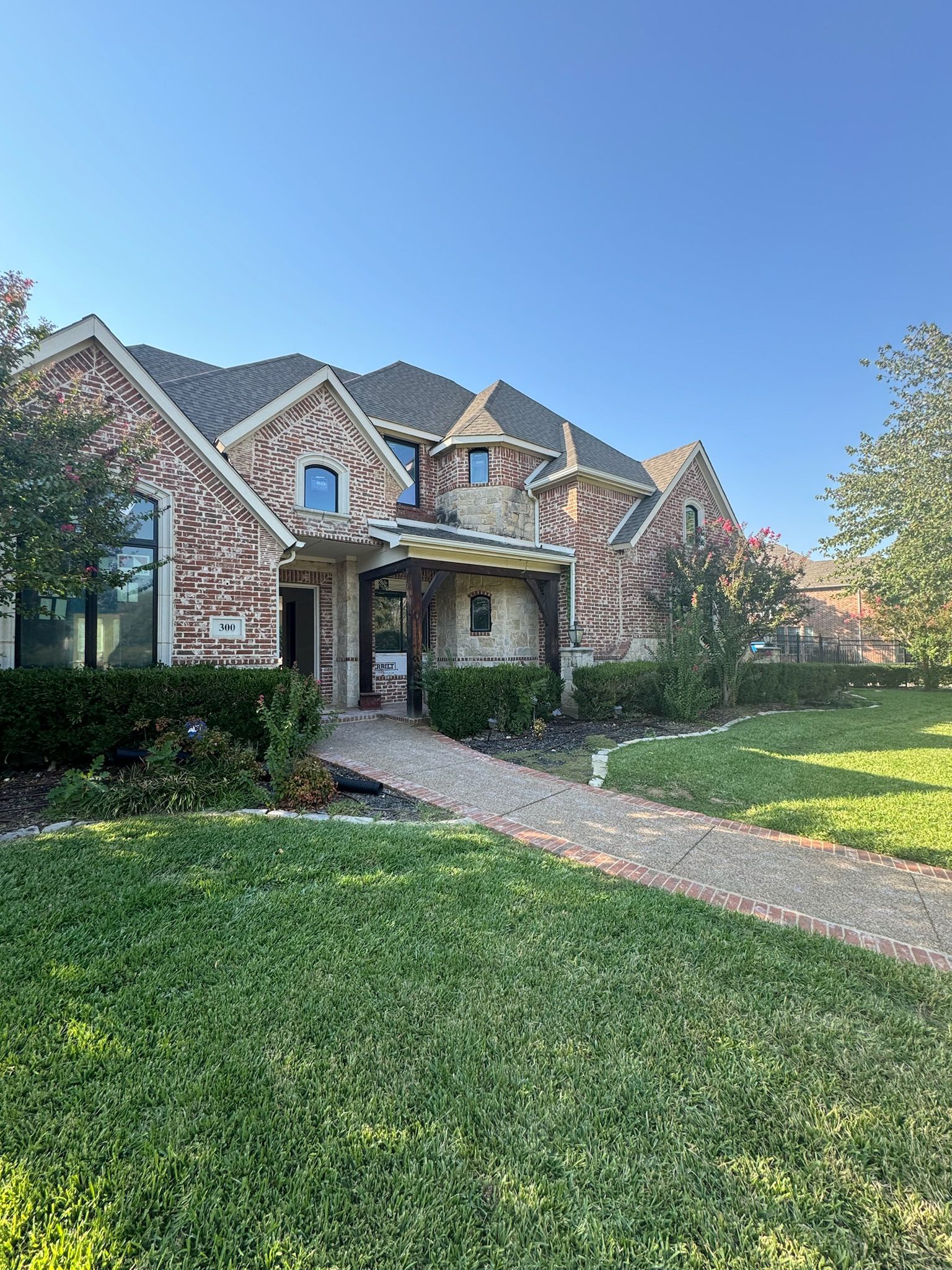 Suburban brick house with arched entry, front walkway, and green lawn under a blue sky