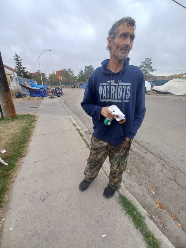 a man wearing a patriots sweatshirt is standing on the sidewalk