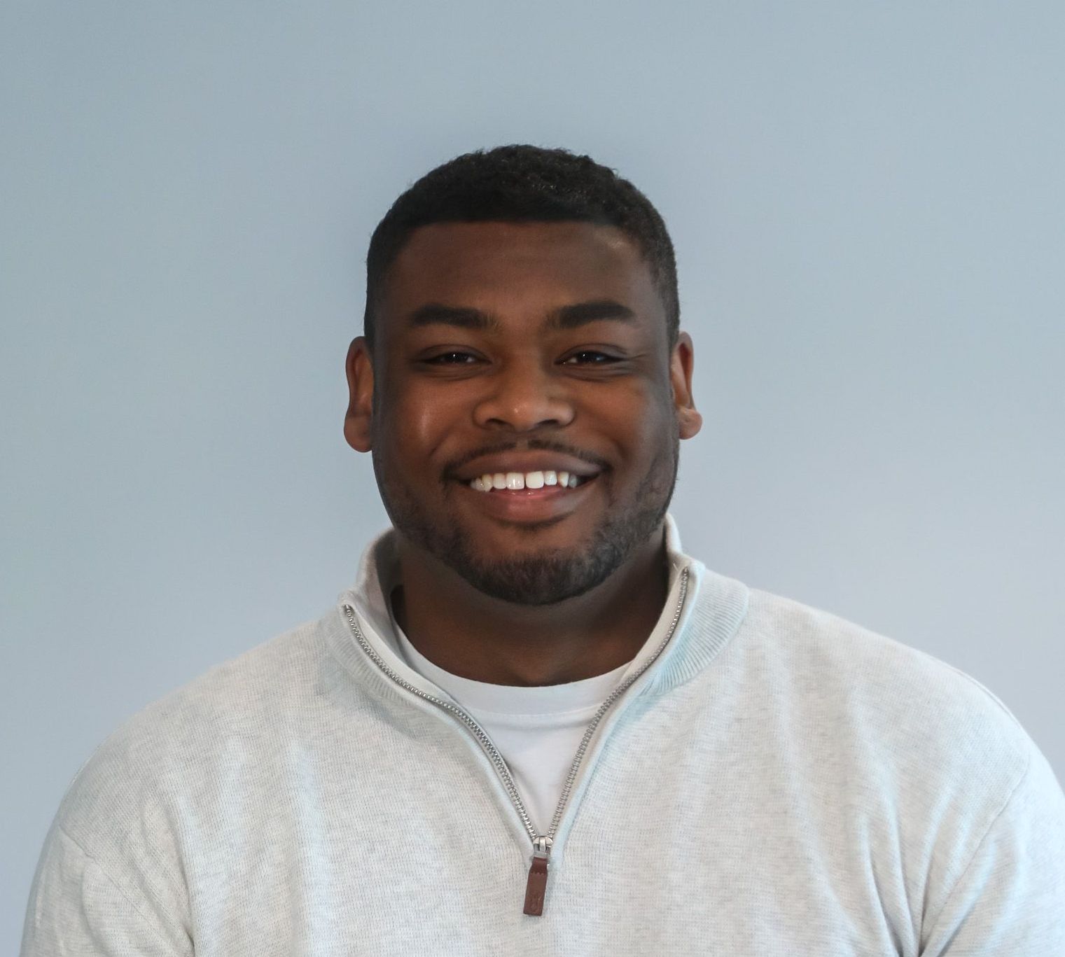 A man with a beard is smiling and wearing a grey sweater
