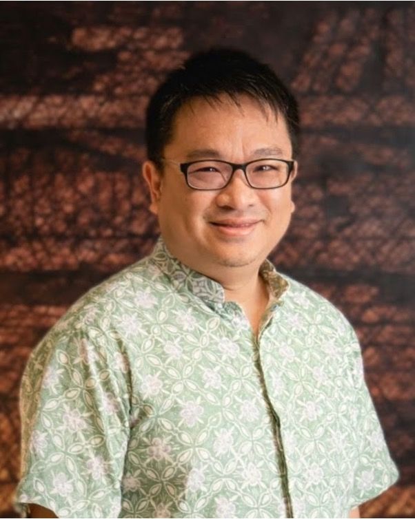 A man wearing glasses and a green shirt is smiling for the camera.