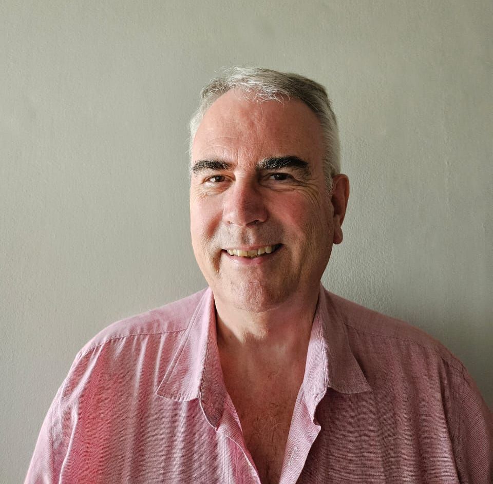 A man in a pink shirt is smiling for the camera.