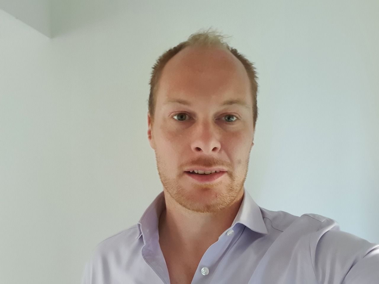 A man with a beard is wearing a purple shirt and smiling for the camera.