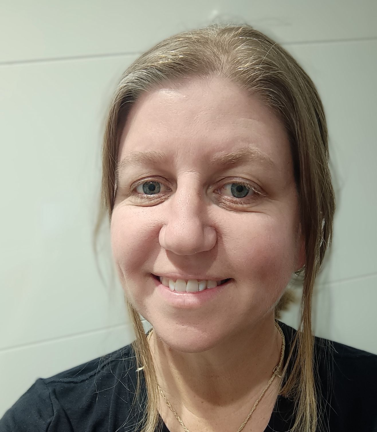 A woman wearing a black shirt and a necklace is smiling for the camera.