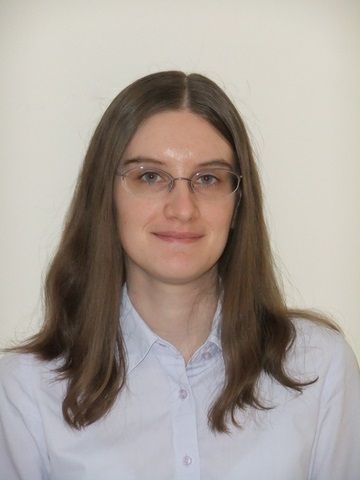 Woman with glasses and long brown hair, wearing a button-down shirt, smiles at the camera.